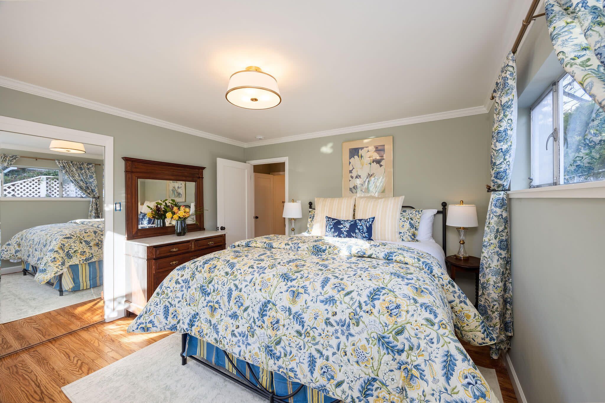 A bedroom with a large bed, a dresser, a mirror, and a window with curtains.