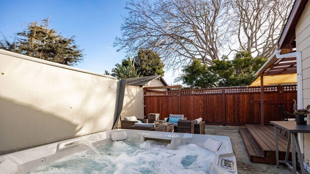 Un jacuzzi en un patio trasero con terraza de madera, mobiliario exterior y cerca de madera.