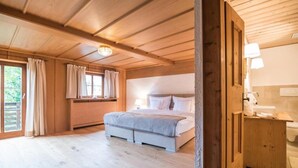 A bedroom with a large bed, wooden ceiling, and a window with curtains. - Apartment HANS - Schusterhäusl (Samerberg)