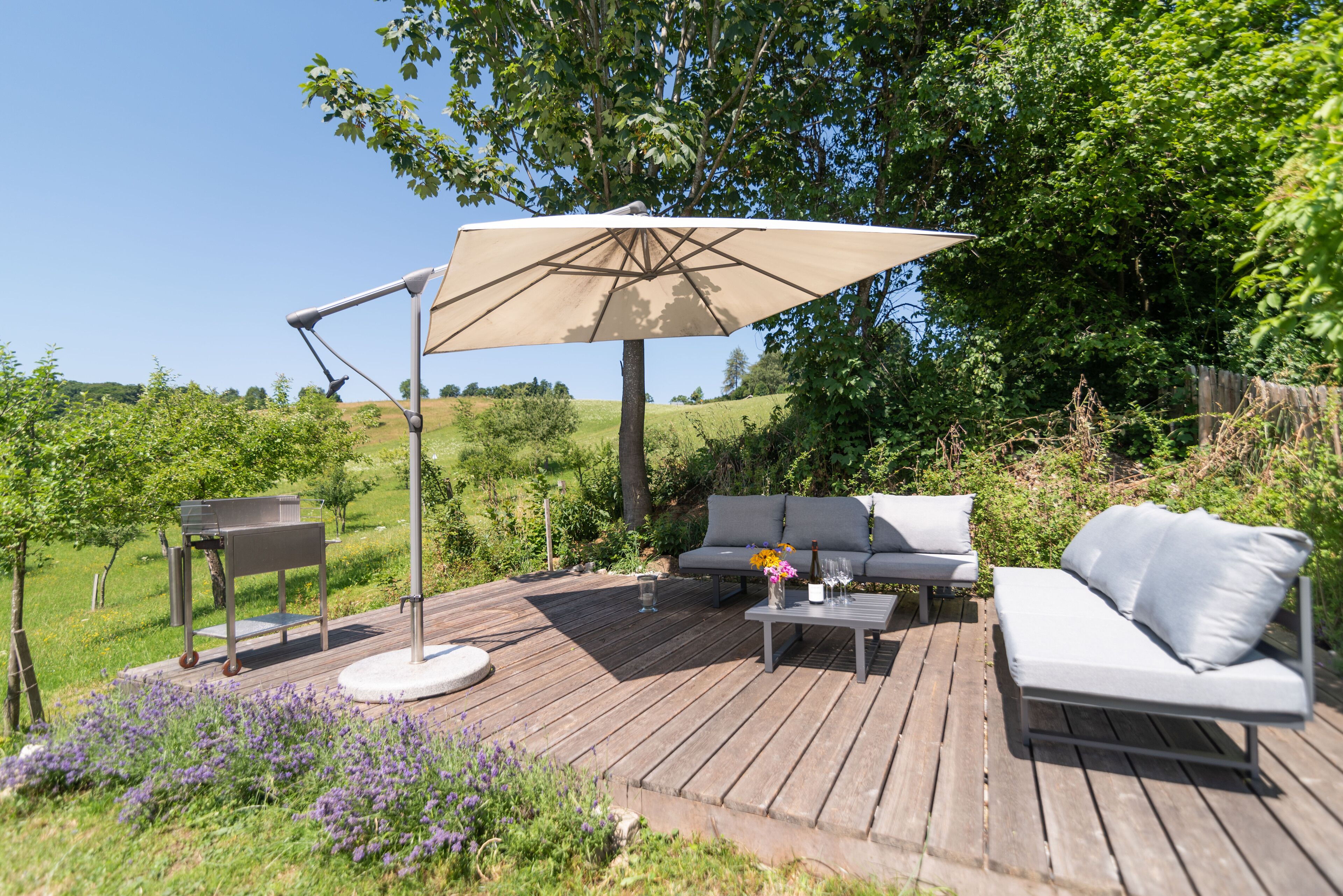 Una terraza de madera con mobiliario exterior, incluyendo un sofá, una mesita de centro y una mesa con lámpara.