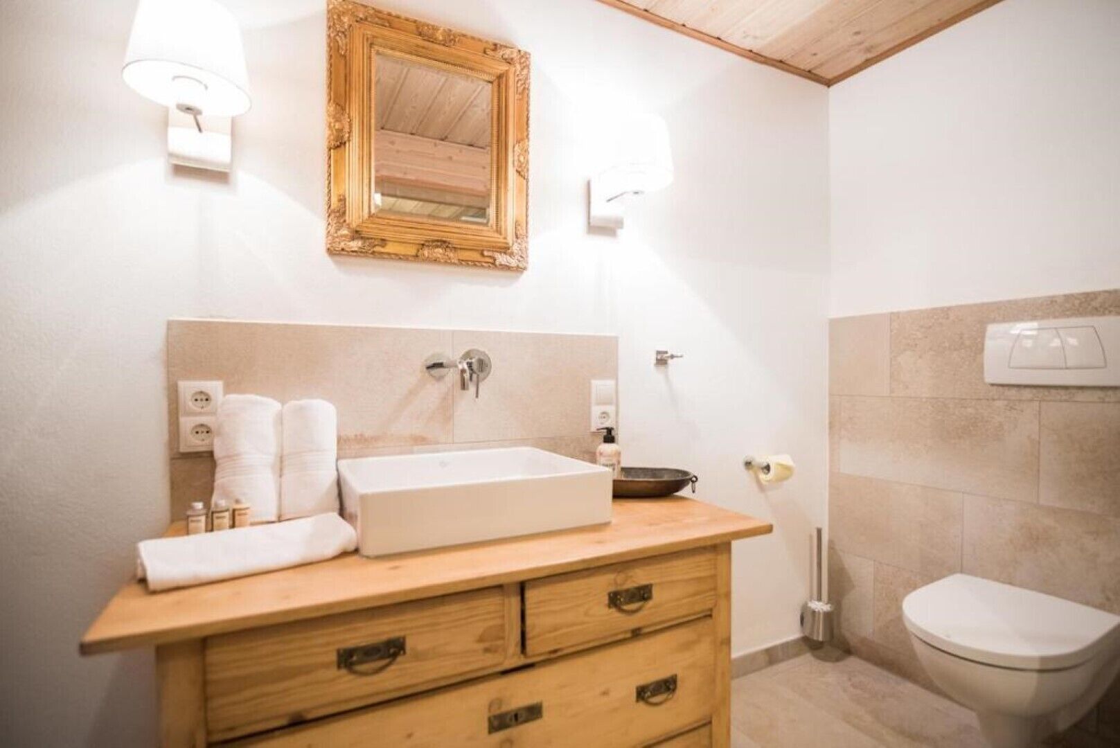 A bathroom with a wooden vanity, a large mirror, a sink, and a toilet.