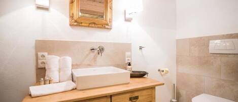 A bathroom with a wooden vanity, a large mirror, a sink, and a toilet.