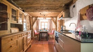 A rustic kitchen with wooden cabinets, a dining table with chairs, and a large window. - Apartment HANS - Schusterhäusl (Samerberg)
