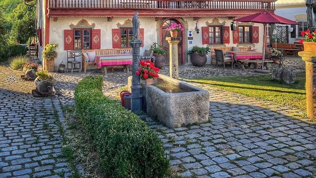 A traditional chalet-style building with a balcony, outdoor seating, and a stone fountain. - Apartment HANS - Schusterhäusl (Samerberg)