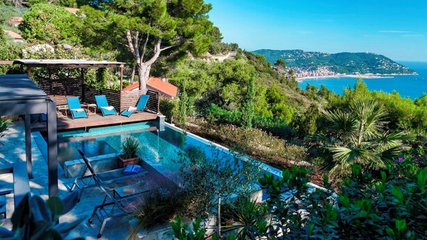 Un espace aménagé au bord de la piscine, avec des chaises longues, une pergola et une vue sur la mer et les collines.