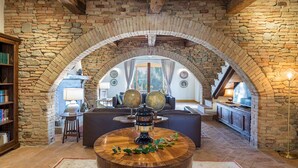 A cozy living room with a stone archway, a round wooden coffee table with decorative globes, a comfortable sofa, and a bookshelf. - Casale Santa Lucia 8+2, Emma Villas (Bettona)