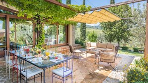 An outdoor dining area with a glass table, chairs, and a cushioned sofa under a pergola. - Casale Santa Lucia 8+2, Emma Villas (Bettona)
