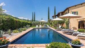 A rectangular pool with lounge chairs and umbrellas, surrounded by well-maintained hedges and plants. - Casale Santa Lucia 8+2, Emma Villas (Bettona)