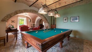 A pool table in a room with brick arches, a billiards rack, and a table with bottles. - La Casa nei Vigneti 10, Emma Villas (Catignano)