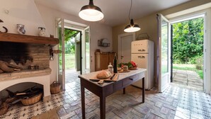 A kitchen with a stone fireplace, wooden table, and hanging lights. - La Casa nei Vigneti 10, Emma Villas (Catignano)