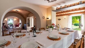 A dining area with a long table set for a meal, an arched doorway leading to another room, and a view of greenery outside. - La Casa nei Vigneti 10, Emma Villas (Catignano)