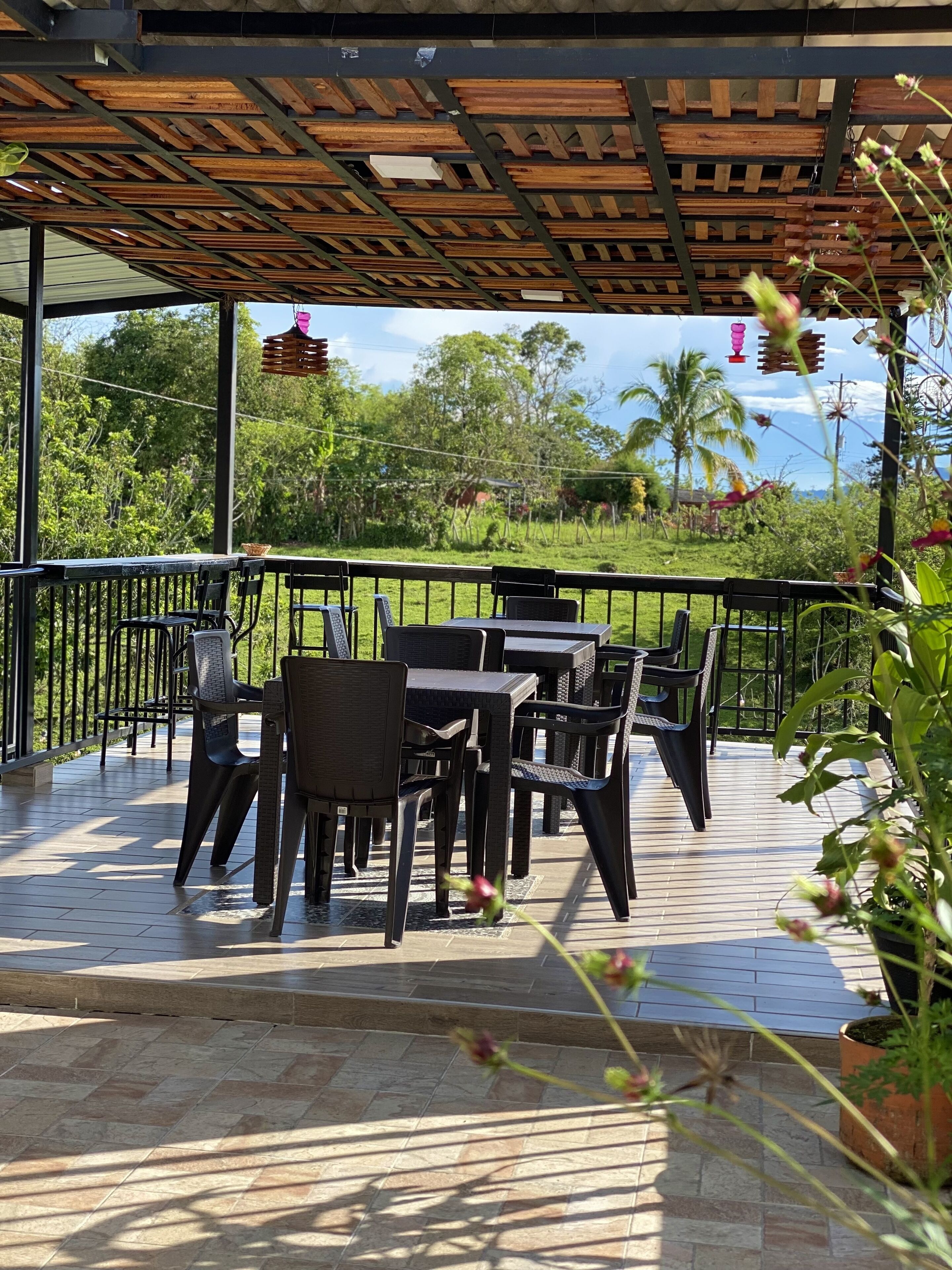 An outdoor patio with wooden tables and chairs, surrounded by a metal railing.