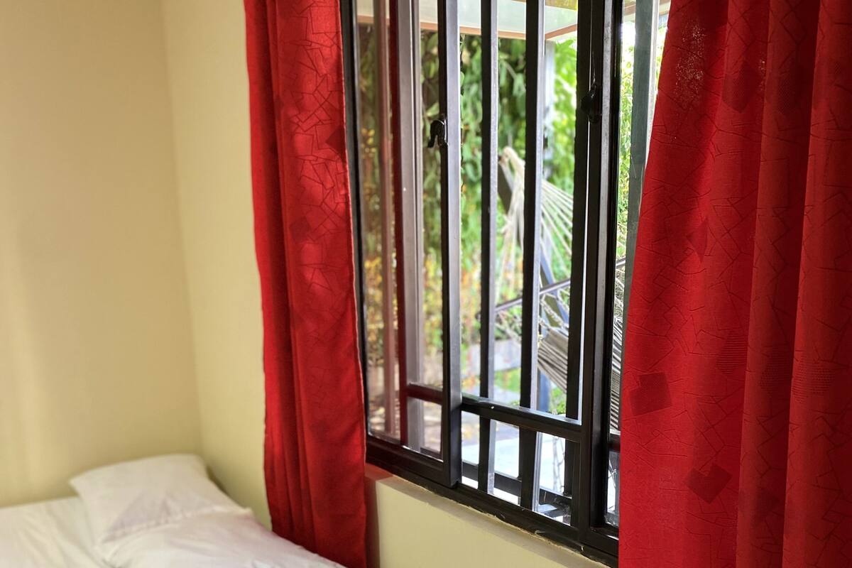 Ein Zimmer mit zwei Einzelbetten, einem Fenster mit Gitterstäben und roten Vorhängen.