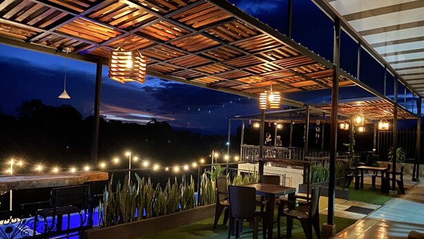 Uma área de varanda externa com mesas, cadeiras, luzes de fadas e piscina.