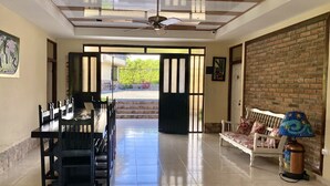 Uma sala de jantar ampla com teto alto, um ventilador de teto e vista para área externa por uma porta grande e aberta.