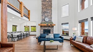 Amplia sala de estar con chimenea de piedra, piso de madera y un alto techo con balcón de madera.