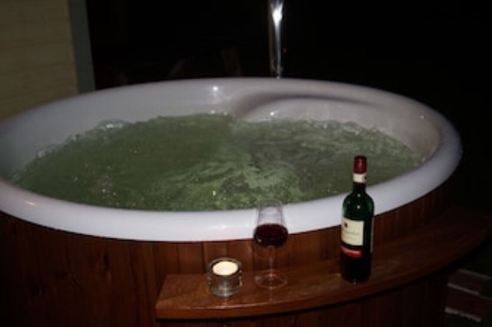 A hot tub filled with water, a bottle of wine, and a glass on a wooden table.