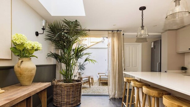 A modern kitchen with a large island, bar stools, a wicker basket with plants, and a view to a dining area.