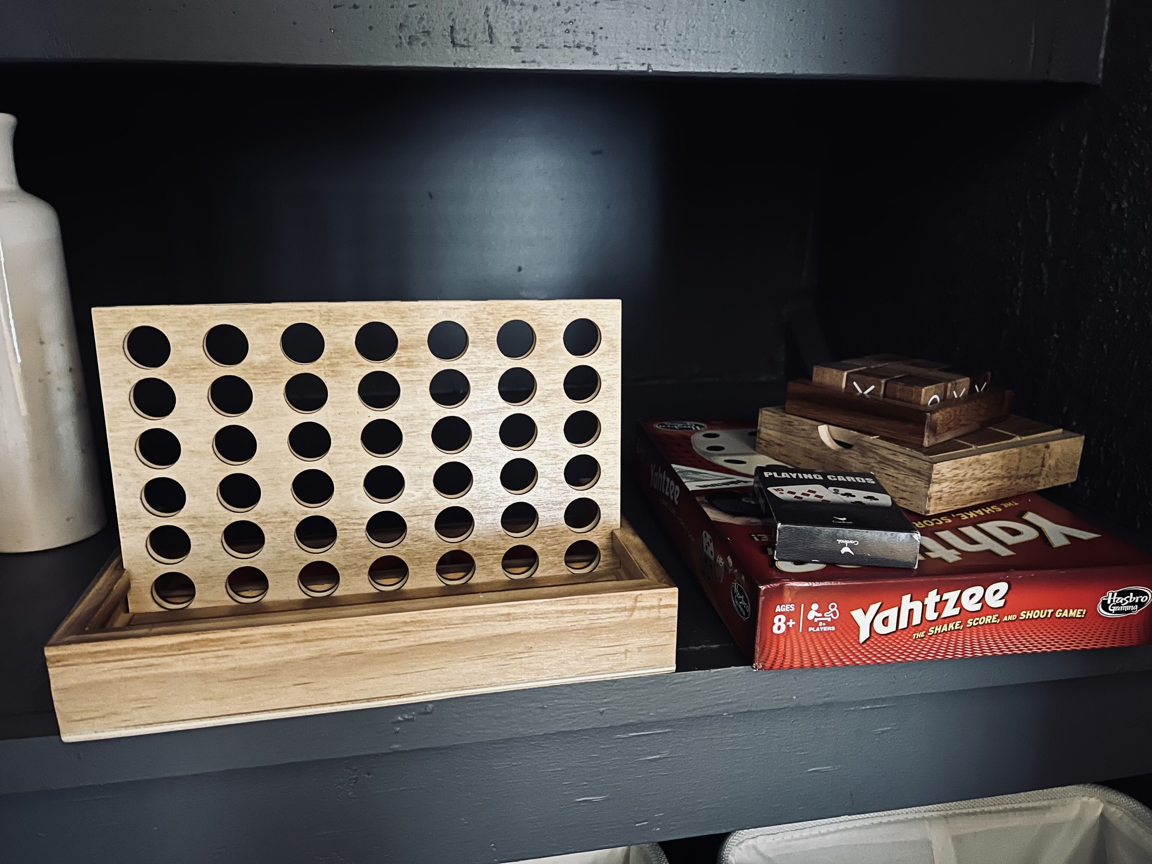 Een plank met een houten pegboard, een witte mok en verschillende Yahtzee speldozen.