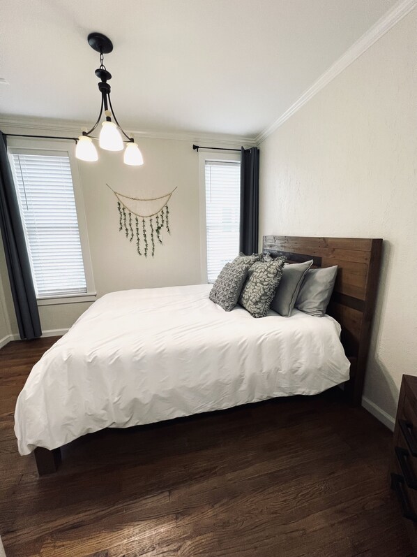 A bedroom with a large bed, wooden headboard, and a hanging light fixture.