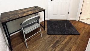 Ein Zimmer mit einem Holztisch, einem Stuhl, einer schwarzen Fußmatte und einer weißen Tür.