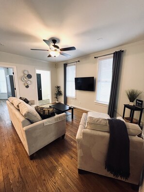 Un salon avec deux canapés, une table basse, un téléviseur et un ventilateur de plafond.