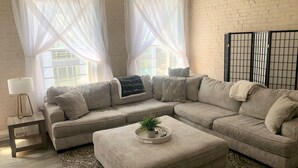 Ein Wohnzimmer mit einem Ecksofa, einem Beistelltisch mit Lampe und einer Dekoschale mit Pflanze.