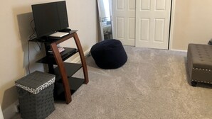 Ein Zimmer mit Fernseher auf einem Holzboden, einem Spiegel, einer Tür und einem gepolsterten Hocker.
