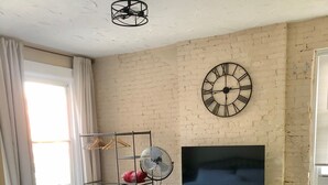 Ein Schlafzimmer mit Bett, Fernseher, einer Uhr, einem Ventilator und einer Kommode.