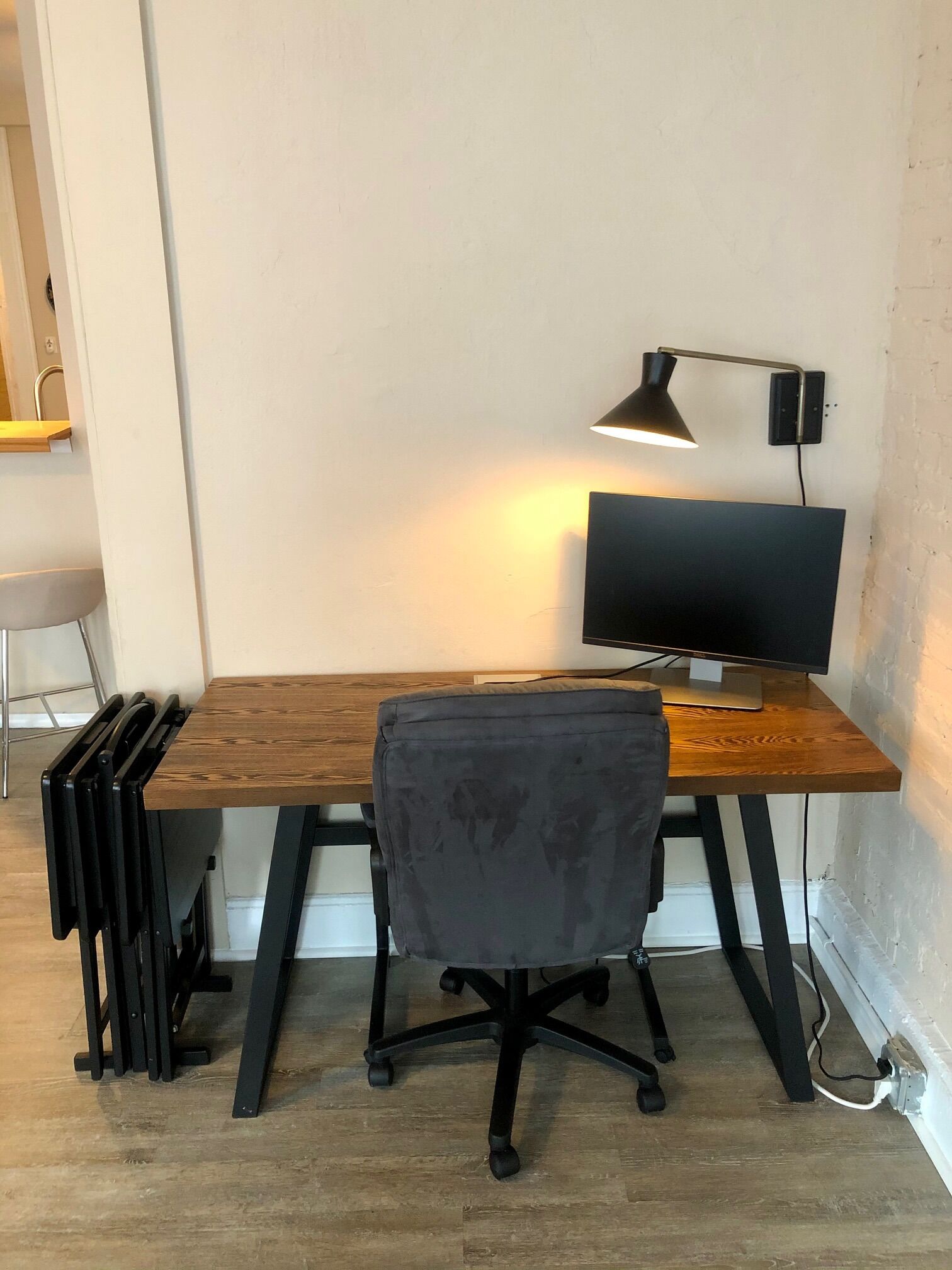 A compact workspace with a wooden desk, a black office chair, a monitor, and a desk lamp.