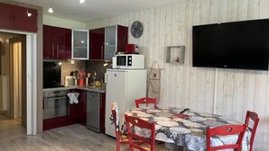 Una cocina compacta con electrodomésticos modernos, una mesa de comedor con sillas rojas y un televisor de pantalla plana montado en la pared.