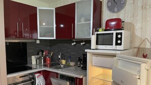 Una cocina compacta con gabinetes rojos, microondas, tostadora y refrigerador.
