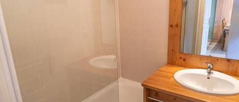 A bathroom with a glass-enclosed shower, a wooden vanity with a sink, and a mirror.
