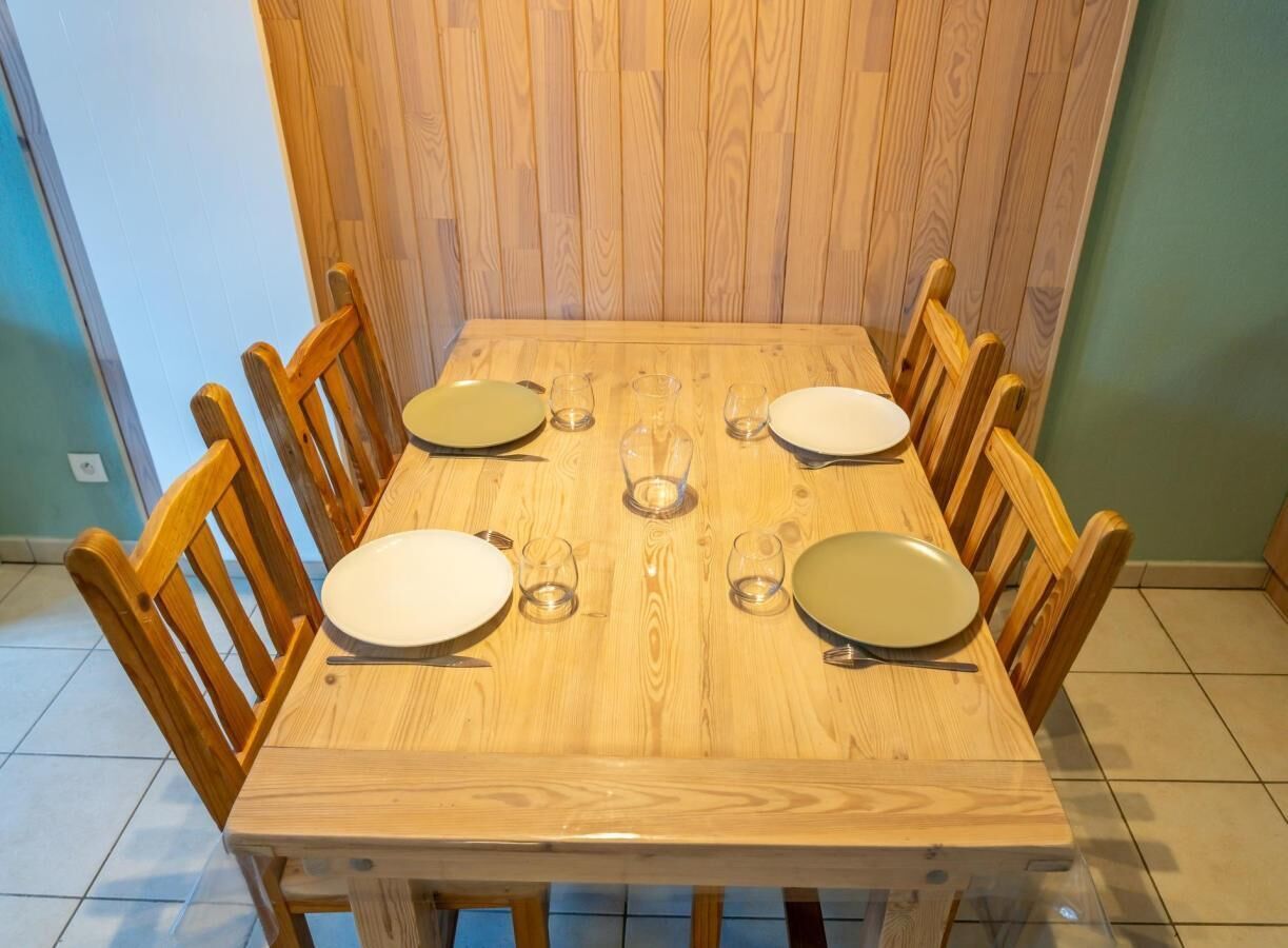 A wooden dining table with six chairs, plates, and glasses set for a meal.