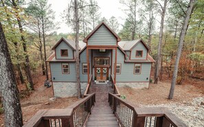A two-story log cabin with a wooden staircase leading to the front door, surrounded by trees. - Creekside, Family-Friendly Cabin w/ Bunk Room (Broken Bow)