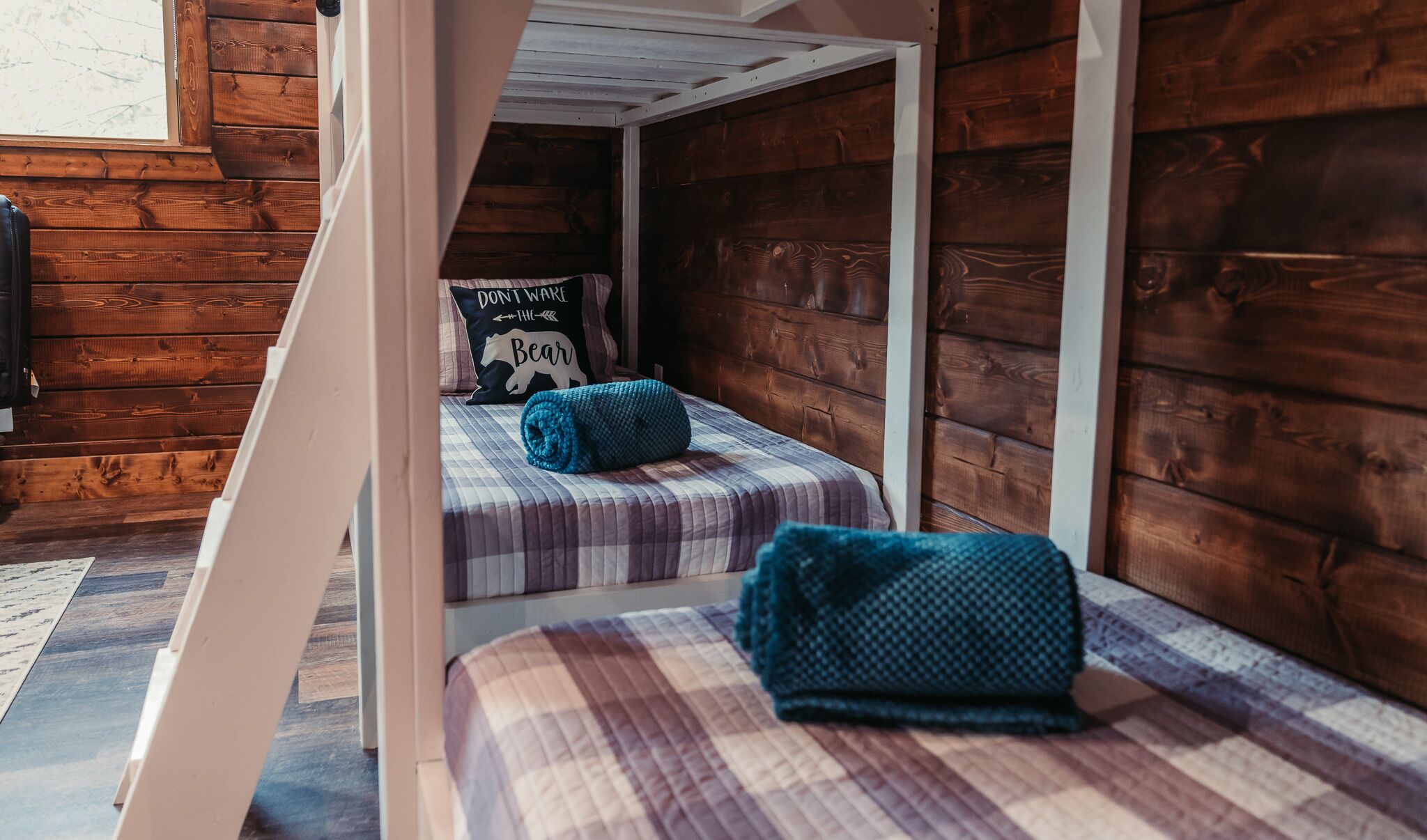 A cozy cabin-style room with two bunk beds, wooden walls, and a window providing natural light.