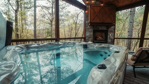 Ein Whirlpool mit Kamin aus Stein, umgeben von einer Holzterrasse und Bäumen.