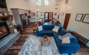 Amplia sala de estar con un sofá azul, chimenea y comedor con muebles de madera.