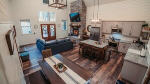 Eine geräumige Küche mit Kamin aus Stein, ein Essbereich mit Holztisch und ein Wohnzimmer mit Sofa und Fernseher.