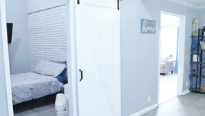 A room with a bed, a white door, a 'home' sign, a bookshelf, and a chair. - The Hidden Gem - Huge Floor Plan - Game Room (Sulphur)