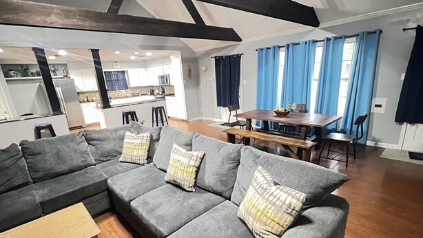 A modern living room with a grey sectional sofa, wooden coffee table, and a dining area with a wooden table and blue curtains. - The Hidden Gem - Huge Floor Plan - Game Room (Sulphur)