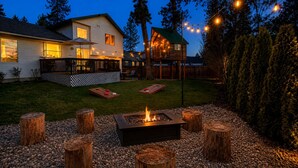 A backyard with a fire pit, wooden stumps, and a deck. - Family Retreat | Treehouse + Game Room | Near Silverwood (Post Falls)