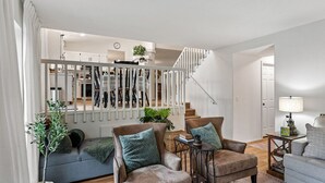 A living room with a staircase, a sofa, armchairs, and a small table with a lamp. - Family Retreat | Treehouse + Game Room | Near Silverwood (Post Falls)