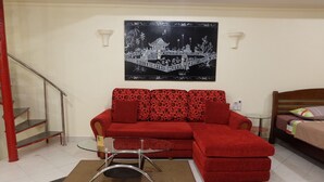 A red sofa with a glass coffee table, a bed with a wooden headboard, a staircase, and a wall-mounted artwork.