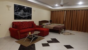 A room with a red sofa, a bed with a brown bedspread, a ceiling fan, and a large black-and-white painting on the wall.