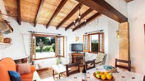 A cozy room with a wooden ceiling, a television, a dining table with a fruit bowl, and a sofa with cushions. - FONTXICA (JUANITO ). Nice and cosy villa (Puerto Pollensa)