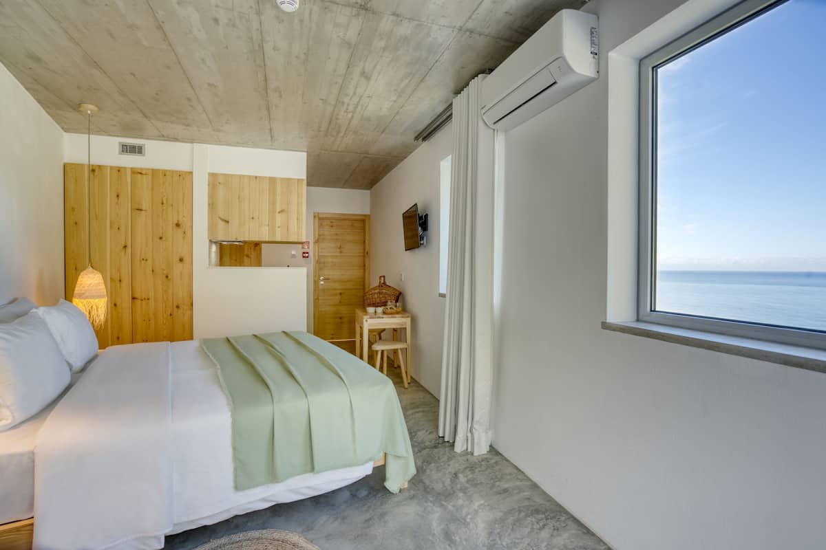 Quarto com cama, paredes de painel de madeira, uma mesinha, televisão e janela com vista.
