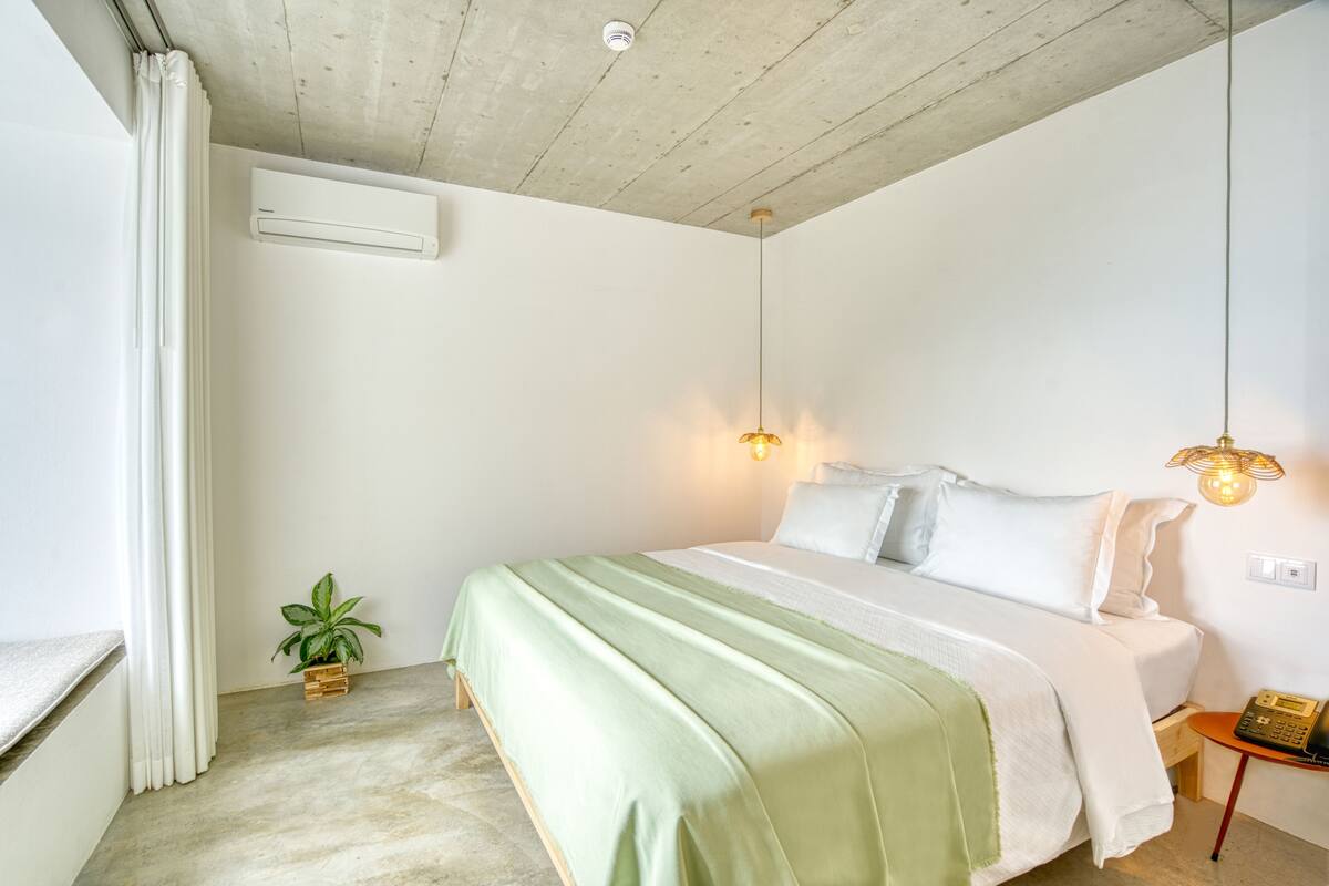 Quarto com cama, mesa de cabeceira, luminária e planta em vaso.