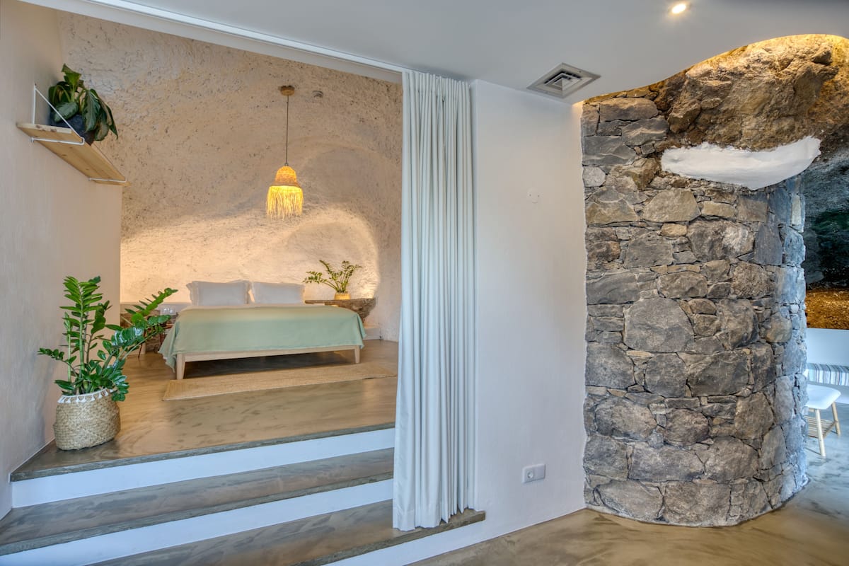 Quarto com parede de pedra, cama, luminária pendente e escada.