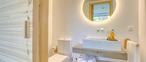 A modern bathroom with a wooden vanity, a round mirror, and a toilet.